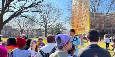 Students gathered around campus preacher, who holds a large yellow sign.