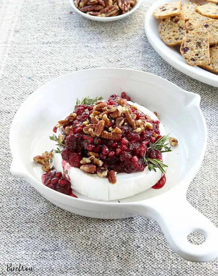 White dish containing brie cheese, cranberries, pomegranate and pecans
