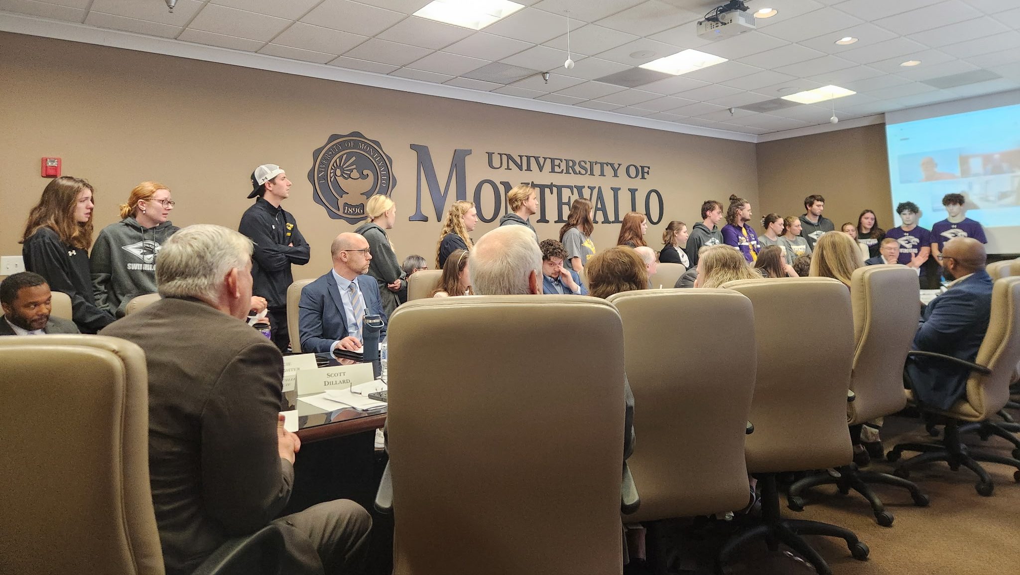Students standing around a conference table where staff and trustees are sitting